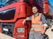 A driver in a high-vis vest leans against the bonnet of a red HGV.