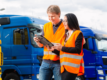 a man and woman, both wearing high-vis, stand in front of a line of blue HGVs consulting a tablet device.